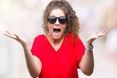 Güzel esmer kıvırcık saçlı Genç kız üzerinde güneş gözlüğü takıyor deli kutluyor arka plan izole ve çığlık kaldırdı ve açık gözleri heyecanlı silah ile başarı için hayrete düşürdü. Kazanan kavramı