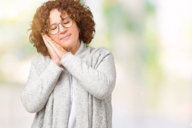 Kapalı gözleri ile gülümseyen iken güzel orta ager kıdemli kadın izole arka plan üzerinde ceket ve gözlük giyen yorgun rüya ve elleri ile poz uyku.