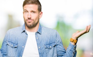 Mavi gözleri ve sakal giyen kot ceket clueless ve kollar ve elleri ile karıştı ifade ile yakışıklı adam kaldırdı. Şüphe kavramı.