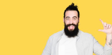 Uzun saç, sakal ve gülümseyen küpe ve boyutu işaret parmaklı ararken ve kamera işi el ile kendine güvenen el hareketi olan genç adam. Ölçü kavramı.