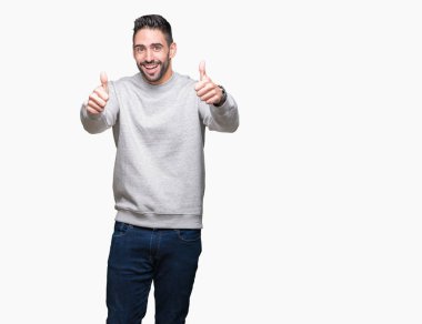 El ile pozitif jest yapıyor izole arka plan başarı işareti üzerinde sweatshirt giyen genç yakışıklı adam başparmak gülümseyen ve mutlu. Neşeli bir ifadeyle, kazanan jest kameraya bakıyor.