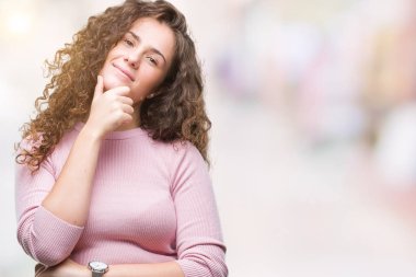 Güzel esmer kıvırcık saçlı Genç kız emin çapraz kollar ve çeneme kaldırdı el ile gülümseme ile kameraya bakarak izole arka plan üzerinde pembe kazak giyiyor. Pozitif düşünce.