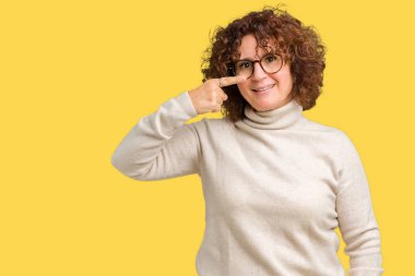 Güzel orta ager kadın kıdemli giyen boğazlı kazak ve gözlük izole üzerinde işaretleme için yüz ve burun, neşeli gülümseyerek el parmak ile arka plan