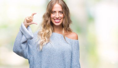 İzole arka plan gülümseyen ve boyutu işaret parmaklı ararken ve kamera işi el ile kendinden emin eller üzerinde kış kazak giyen güzel genç sarışın kadın. Ölçü kavramı.