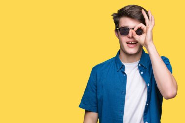 Yakışıklı delikanlı gülümseyen, parmakları ile mutlu yüz üzerinden seyir göz el ile ok jest yapıyor izole arka plan üzerinde güneş gözlüğü takıyor.