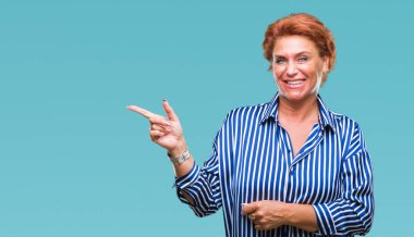 Yüzünde kocaman bir gülümseme ile izole arka plan Atrractive üst düzey beyaz Kızıl saçlı kadın kameraya bakarak yan el ve parmak ile işaret.