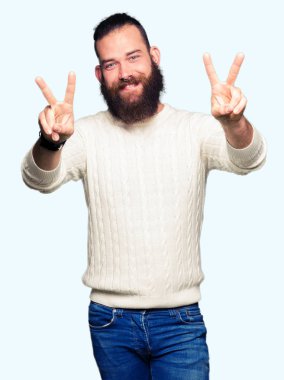 Zafer işareti yapıyor parmak gösterilen kamera seyir gülümseyen genç hipster adam giyen kış kazak. İki numaralı.