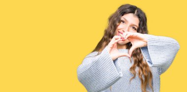 Kalp simgesi ve elleriyle şekil gösterilen aşık gülümseyen kış kazak giyen genç güzel kadın. Romantik kavramı.