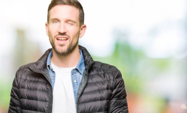 Yakışıklı adam seksi ifade, neşeli ve mutlu yüz ile kamera bakarak kış ceket göz kırpıyor giyiyor.