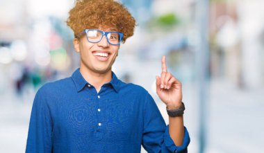 Afro saçlı mavi giyen genç yakışıklı adam başarılı fikri ile işaret parmağını gözlük. Çıktıktan ve mutlu. Bir numara.