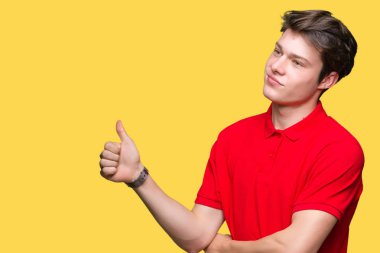 Kırmızı giyen genç yakışıklı adam yanına bir jest yapıyorsun gülümseyen t-shirt gurur, seyir izole arka plan üzerine yaşasın