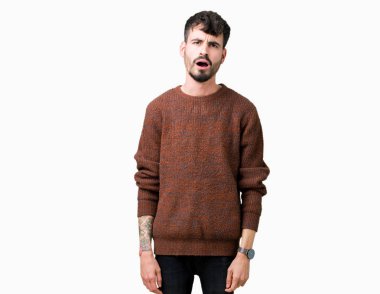 Şüpheci ve alaycı, şok karşısında izole arka plan üzerinde kış kazak giyen genç yakışıklı adam açık ağız ile şaşırttı