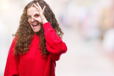 Güzel esmer kıvırcık saçlı genç kız gülümsüyor, parmakları ile mutlu yüz üzerinden seyir göz el ile ok jest yapıyor izole arka plan üzerinde gözlük ve kış kazak giyiyor.