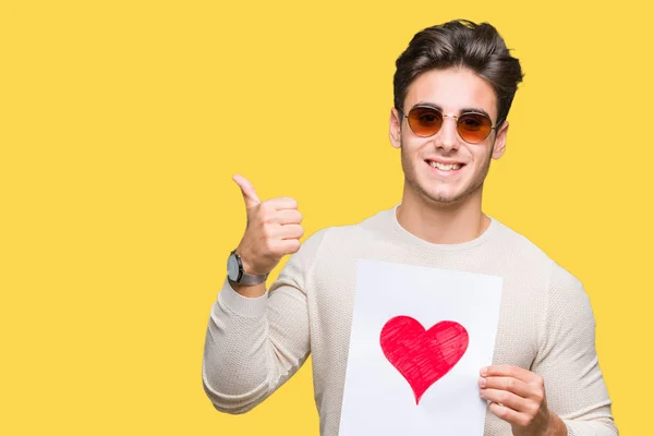 Joven Hombre Guapo Sosteniendo Tarjeta Con Corazón Rojo Sobre Fondo — Foto de Stock