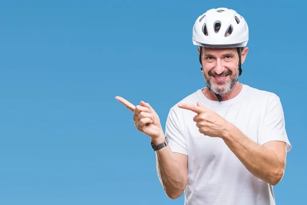 Middle age senior hoary cyclist man wearing bike safety helment isolated background smiling and looking at the camera pointing with two hands and fingers to the side.