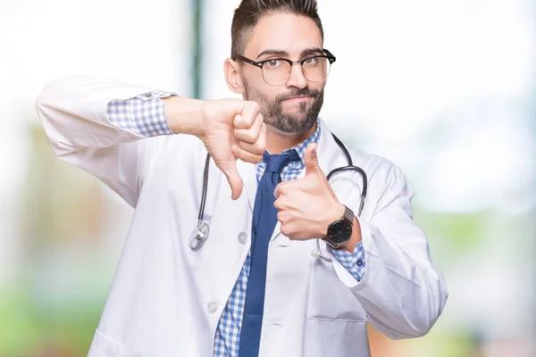 Handsome young doctor man over isolated background Doing thumbs up and down, disagreement and agreement expression. Crazy conflict