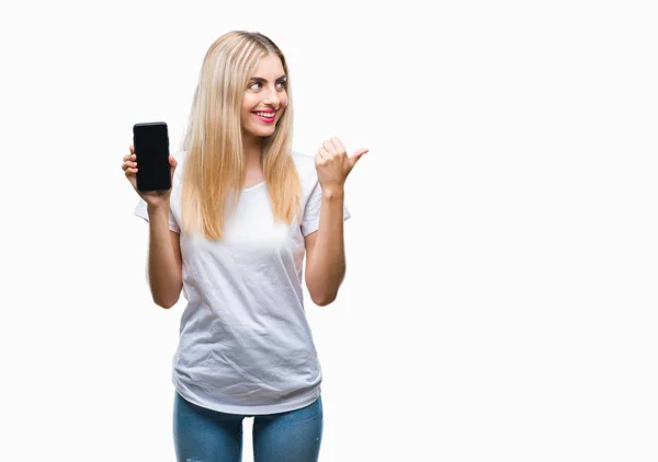 年轻美丽的金发碧眼的女人展示智能手机在孤立的背景指向和显示与快乐的脸微笑的一侧与拇指 — 图库照片