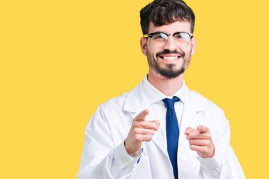 Fotoğraf makinesi ile mutlu ve komik yüz için parmakları işaret izole arka plan üzerinde beyaz önlük giyen genç profesyonel bilim adam. İyi enerji ve vibes.