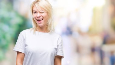 Seksi bir ifadeyle, neşeli ve mutlu yüzünü kameraya bakarak göz kırpıyor izole arka plan üzerinde beyaz t-shirt giyen genç güzel sarışın kadın.