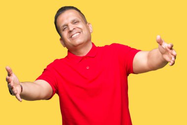 Orta yaş Arap adam izole arka plan sarılmak için kollarını açarak gülümseyen kamera bakıyor. Neşeli ifade kucaklayan mutluluk.