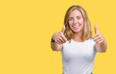 El ile pozitif jest yapıyor onaylama izole arka plan üzerinde rahat beyaz t-shirt giyen güzel ve genç birbayan başparmak gülümseyen ve başarı için mutlu. Kamera, kazanan jest arıyorsunuz.