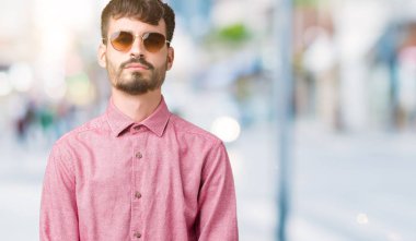 Genç yakışıklı adam yüzünde ciddi bir ifade ile izole arka plan üzerinde güneş gözlüğü takıyor. Basit ve doğal kameraya bakıyor.