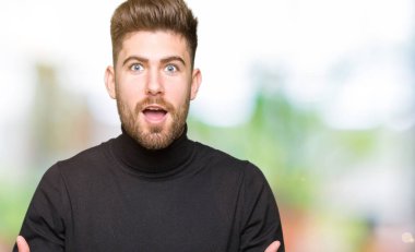 Genç yakışıklı sarışın adam kış kazak korkuyor ve sürpriz ifade, korku ve heyecanlı yüz ile şok giyiyor.