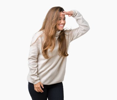 Üzerinde boğazlı kazak giyen genç güzel esmer kadın arka plan çok mutlu ve gülümseyen uzakta el ile üzerine kafa seyir izole. Arama kavramı.