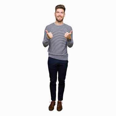 Yakışıklı delikanlı çizgili süveter başarı işareti el ile olumlu hareketi yaparken giyiyor başparmak gülümseyen ve mutlu. Neşeli bir ifadeyle, kazanan jest kameraya bakıyor.