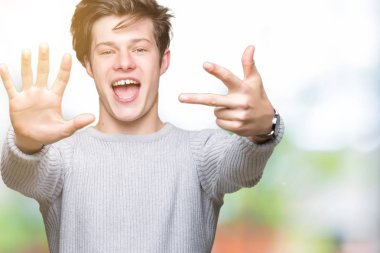 Gösterilen arka plan üzerinde kış kazak giyen genç yakışıklı adam izole ve parmakları ile işaret kendinden emin ve mutlu gülümseyerek süre 8 numaralı.