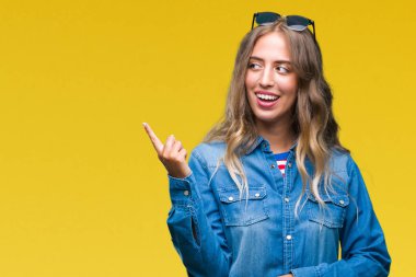 Kameraya bakarak yan el ve parmak ile işaret yüzünde kocaman bir gülümseme ile izole arka plan üzerinde güneş gözlüğü takıyor güzel sarışın genç kadın.