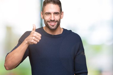 Hareketi el ile mutlu yaşasın yapıyor izole arka plan üzerinde kazak giyen genç yakışıklı adam. Başarı gösteren kameraya bakarak ifade onaylama.