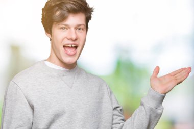 Neşeli sunulması ve kameraya bakarak avucunun ile işaret gülümseyen izole arka plan üzerinde sweatshirt giyen genç yakışıklı sportif adam.