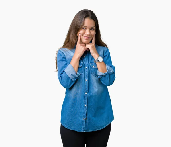 若い美しいブルネットの女性身に着けている青いデニム シャツ分離上背景笑顔口を開けて 指を指すと 陽気な笑顔を強制 — ストック写真