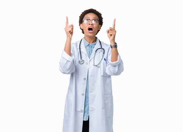年轻的非洲医生妇女穿着医疗外套在孤立的背景惊讶和惊讶地抬起头来 用手指指指点点 举起双臂 — 图库照片