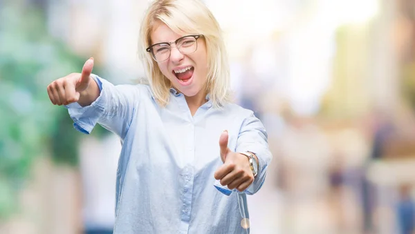 Young beautiful blonde business woman wearing glasses over isolated background approving doing positive gesture with hand, thumbs up smiling and happy for success. Looking at the camera, winner gesture.