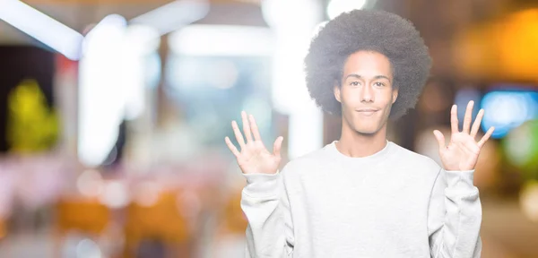 アフロの髪を指でスポーティなスウェット シャツ表示とポイントを着ての若いアフリカ系アメリカ人は自信を持って 幸せな笑みを浮かべている間 数します — ストック写真