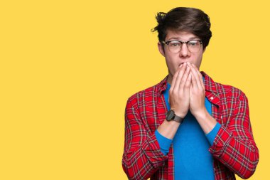 İzole arka plan üzerinde gözlük giyen genç yakışıklı öğrenci adam yanlışlık için eller ile ağız kapsayan şok. Gizli konsept.