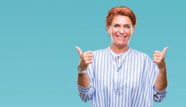 Atrractive üst düzey beyaz Kızıl saçlı kadın izole arka plan başarı işareti başparmak gülümseyen ve mutlu el ile olumlu hareketi yapıyor. Neşeli bir ifadeyle, kazanan jest kameraya bakıyor.