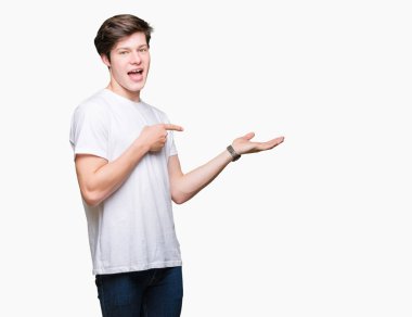 Hayret ve el ile sunulması ve parmak ile işaret ederken kameraya gülümseyen izole arka plan üzerinde rahat beyaz t-shirt giyen genç yakışıklı adam.