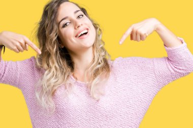 Yüzünde gülümseme ile kendinden emin görünüyorsun, kendini gururlu ve mutlu parmakları ile işaret izole arka plan üzerinde sarışın güzel genç kadın.