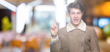 Yüz üzerinde büyük bir gülümseme ile izole arka plan üzerinde kış ceket giyen genç yakışıklı adam, kamera bakarak yan el ve parmak ile işaret.