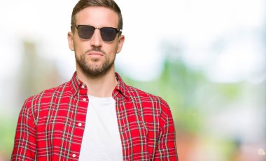Yüzünde ciddi bir ifade ile moda güneş gözlüğü giyen yakışıklı adam. Basit ve doğal kamera bakıyor.