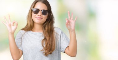 Genç güzel esmer kadın giyiyor güneş gözlüğü izole arka plan üzerinde dinlenmek ve gülümseyen gözlerle kapalı parmak jestle meditasyon yapıyor. Yoga kavramı.