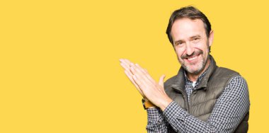 Orta yaş yakışıklı adam giyen kış yelek Clapping ve mutlu ve neşeli, gururlu gülümseyen eller birlikte alkış