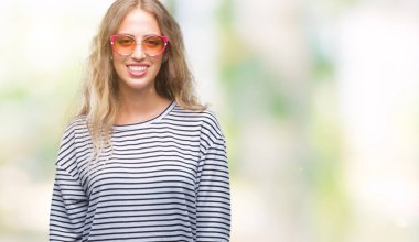 Yüzünde mutlu ve güzel bir gülümseme ile izole arka plan üzerinde güneş gözlüğü takıyor güzel sarışın genç kadın. Şanslı kişi.