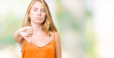 Mutsuz ve kızgın ret gösterilen ve başparmak aşağı hareketi ile negatif seyir izole arka plan üzerinde turuncu gömlek giymiş güzel ve genç birbayan. Kötü ifade.