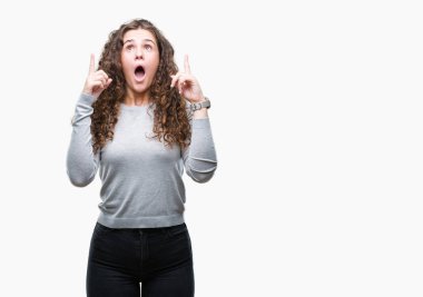 Güzel esmer kıvırcık saçlı Genç kız izole arka plan üzerinde bir kazak giyiyor hayret ve yukarıya bakıp parmakları ile işaret şaşırttı ve silah kaldırdı.