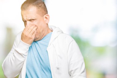 Orta Çağ Arap adam izole arka plan üzerinde sweatshirt giyen bir şey kokmuş ve mide bulandırıcı koku, burnunu parmaklar ile nefes tutan kokuyor. Kötü koku kavramı.