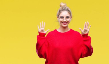 Gösterilen ve parmakları ile işaret izole arka plan üzerinde kırmızı kazak ve gözlük giyen genç güzel sarışın kadın kendinden emin ve mutlu gülümseyerek süre on numara.
